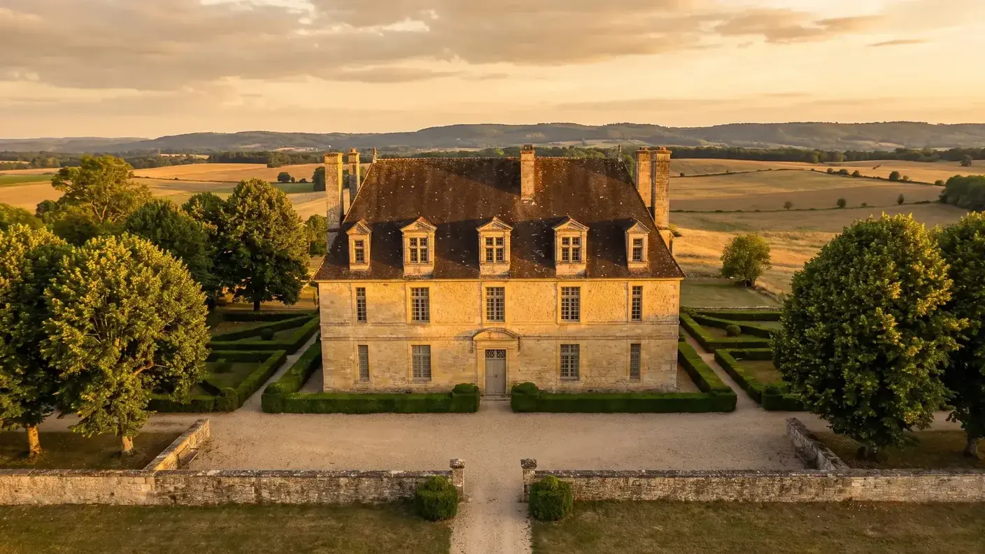 Le château de Burée près de Bertric-Burée, manoir des XVIIe-XVIIIe siècles à façade de pierre dorée, lucarnes et jardin de buis, dans la campagne au couchant