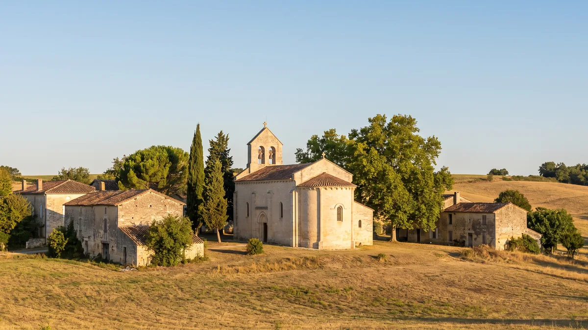 Une petite église de village du Lot-et-Garonne en pierre claire, clocher-mur, entourée de maisons de pierre et de cyprès