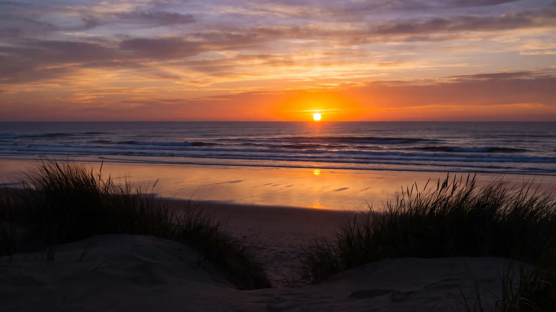 Le soleil couchant fondant dans l'Atlantique, plage mouillée miroir de l'embrasement, dunes en silhouette