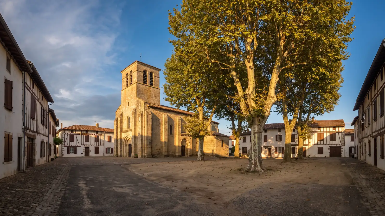 Une église de pierre au solide clocher carré et des maisons basses landaises autour d'une place ombragée