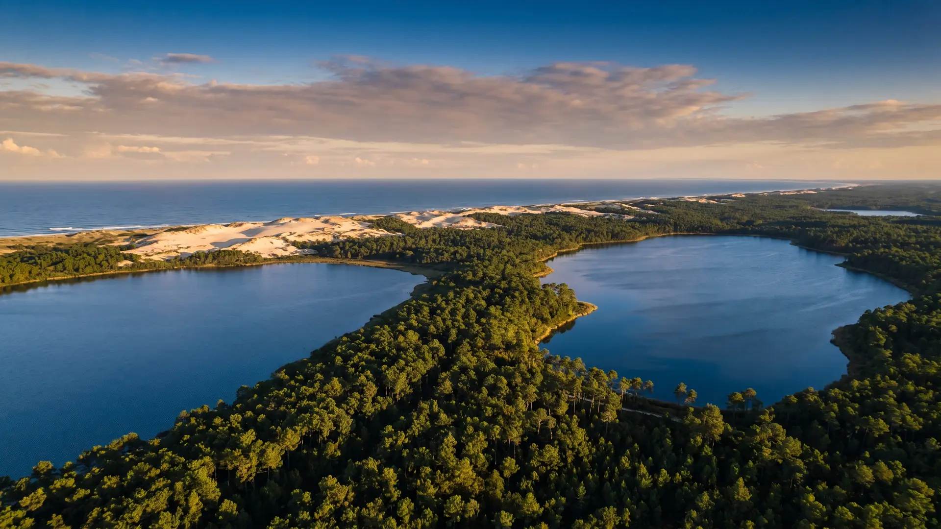 Deux immenses lacs bleus séparés par une langue de forêt de pins, la ligne des dunes et l'océan au loin