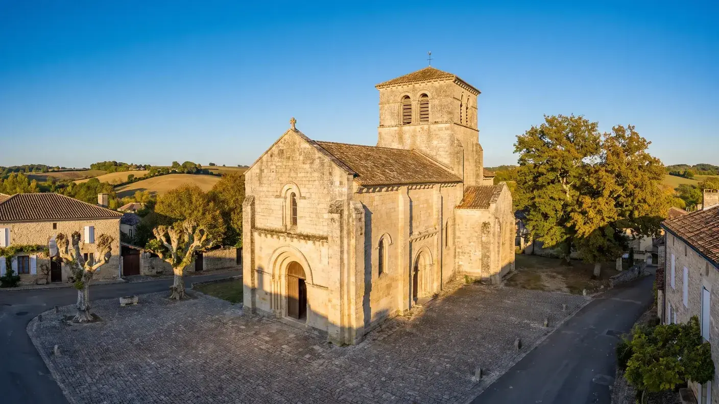 Une église romane du XIIe siècle en pierre grise en Charente, portail en plein cintre, clocher carré à baies géminées