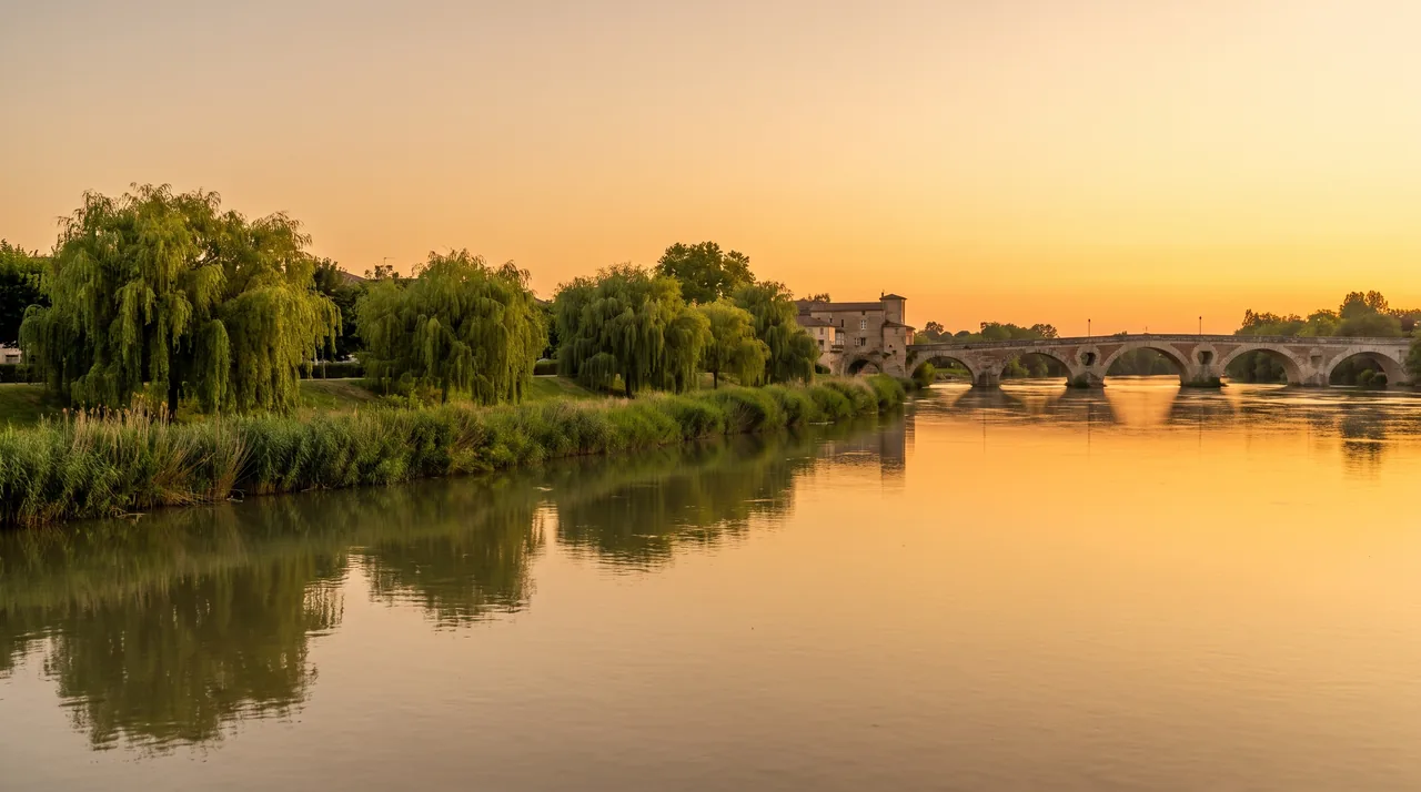 La Garonne large et calme au soleil couchant près de Cadillac, berges boisées et pont métallique au loin