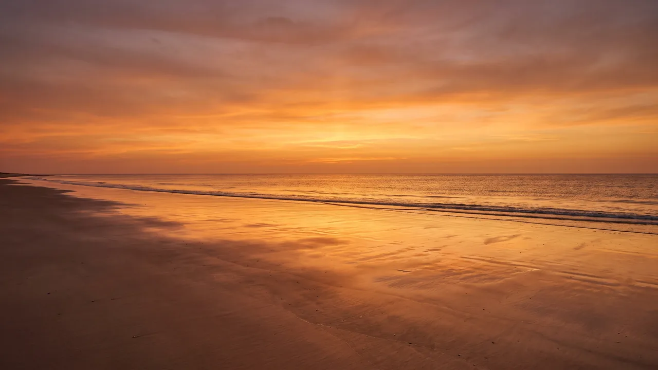 Coucher de soleil orangé sur l'Atlantique depuis une plage déserte de Carcans, sable humide réfléchissant le ciel chaud