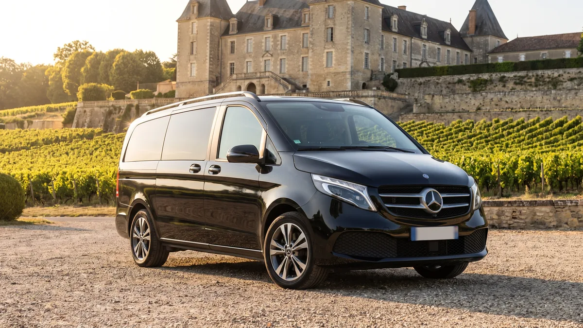 Van noir avec chauffeur stationné devant un château viticole du vignoble bordelais