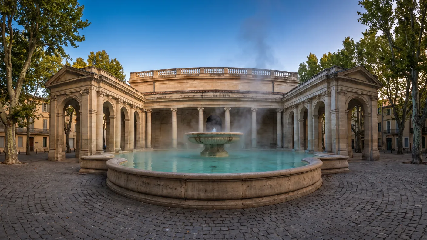 La Fontaine Chaude de Dax et son bassin thermal fumant sous les colonnes néoclassiques, à l'aube