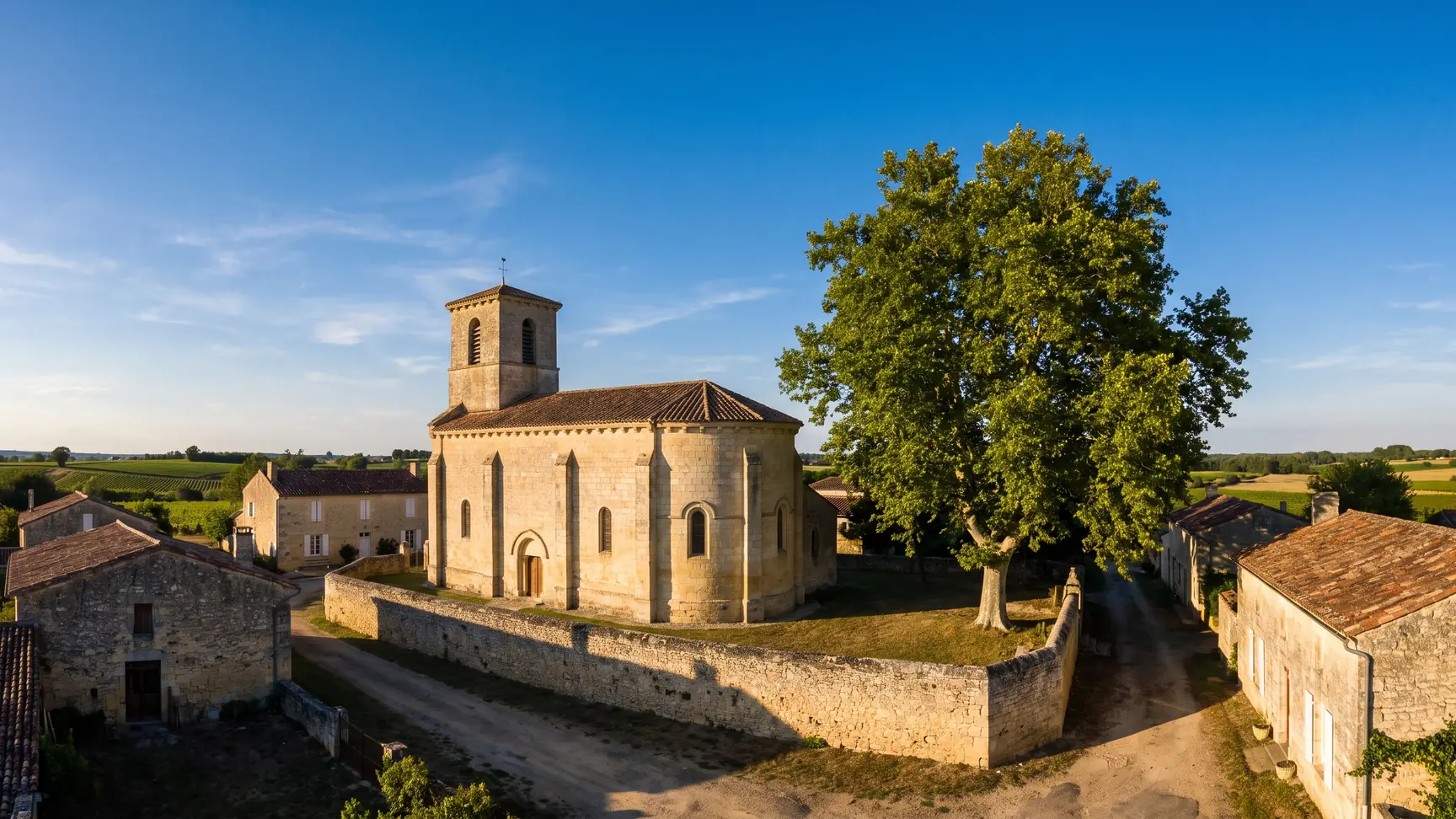 Une petite église de village en pierre claire à clocher carré, entourée de maisons basses à toits de tuiles