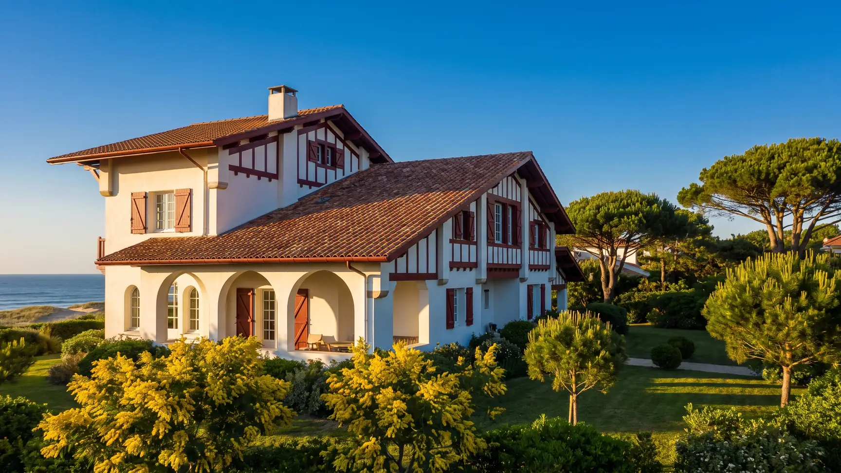 Une élégante villa basco-landaise des années 1920 aux murs blancs et colombages rouge sombre, jardin de pins