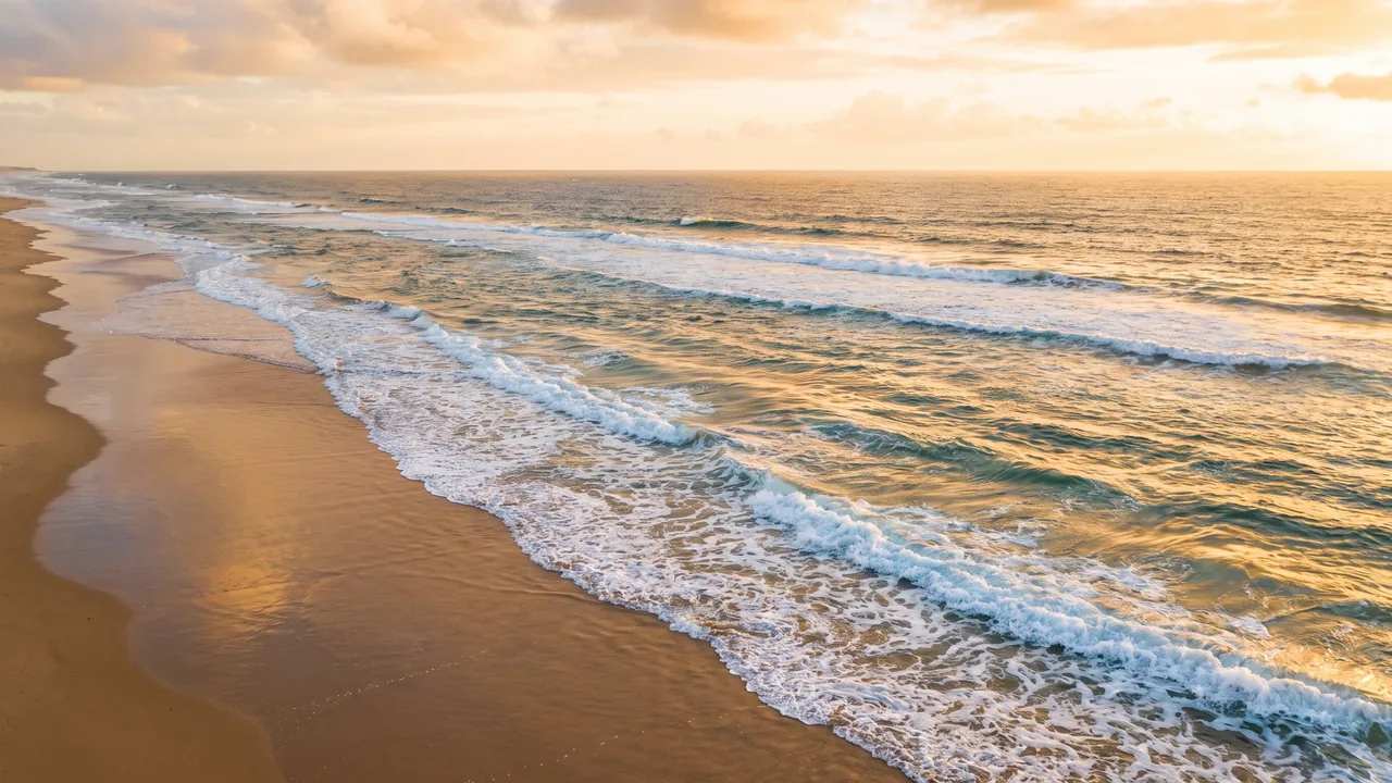 Longues lignes de houle atlantique déferlant en écume sur une plage déserte d'Hourtin au soleil couchant, eau turquoise