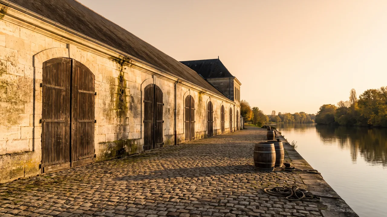 Longue façade de pierre claire d'un chai de vieillissement du cognac à Jarnac, hautes portes cintrées et toit de tuiles