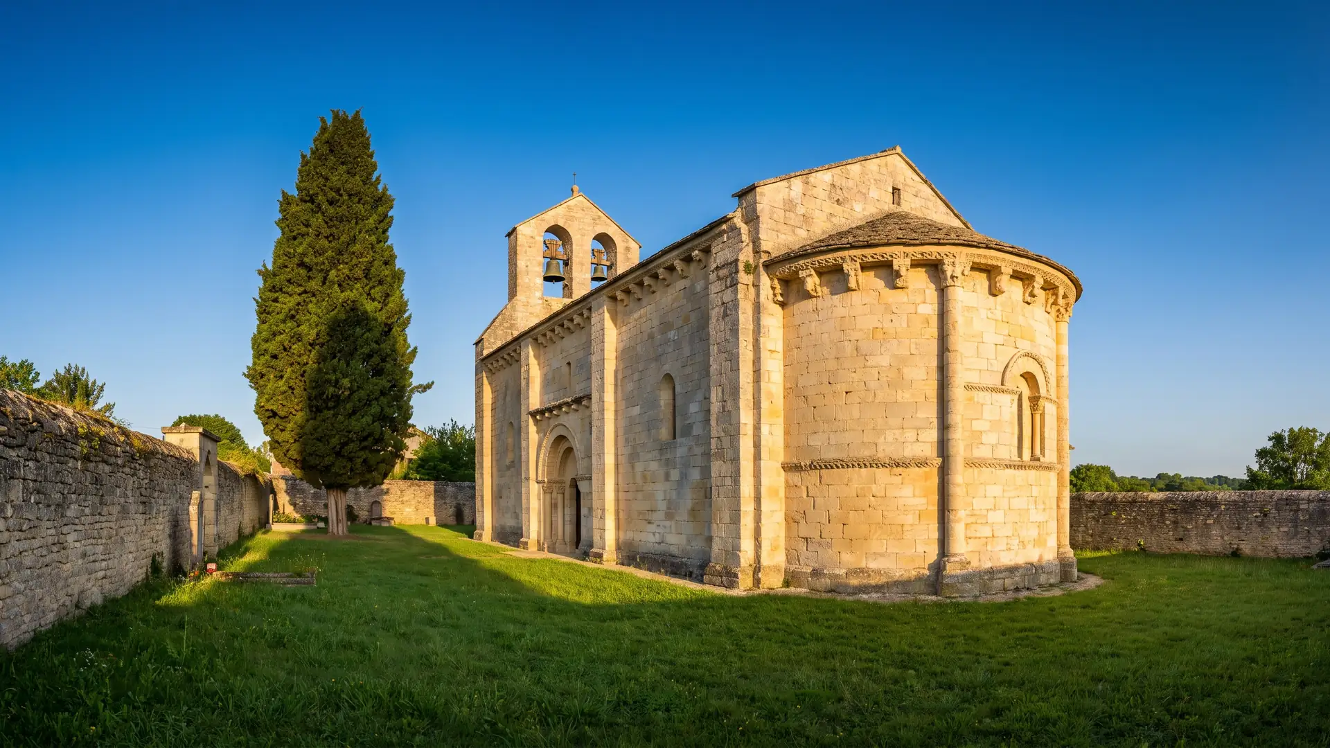 Une église romane de village en pierre couleur de miel, chevet arrondi à corbeaux sculptés et clocher-mur