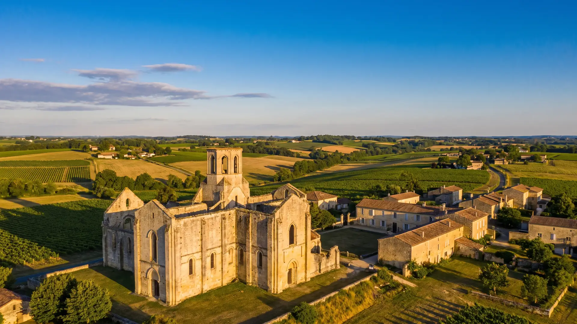 Un panorama des ruines d'une abbaye romane au milieu des vignes de l'Entre-deux-Mers, coteaux, hameaux et bois