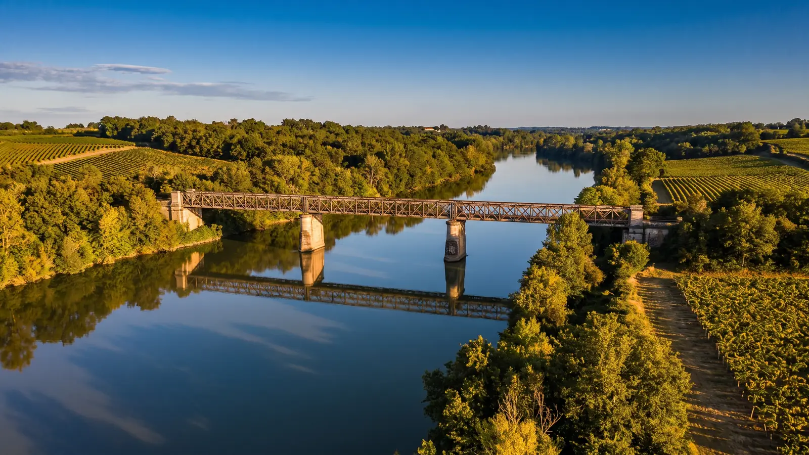 La Garonne à l'heure dorée, un fleuve calme franchi par un élégant pont métallique du XIXe siècle, coteaux de vignes