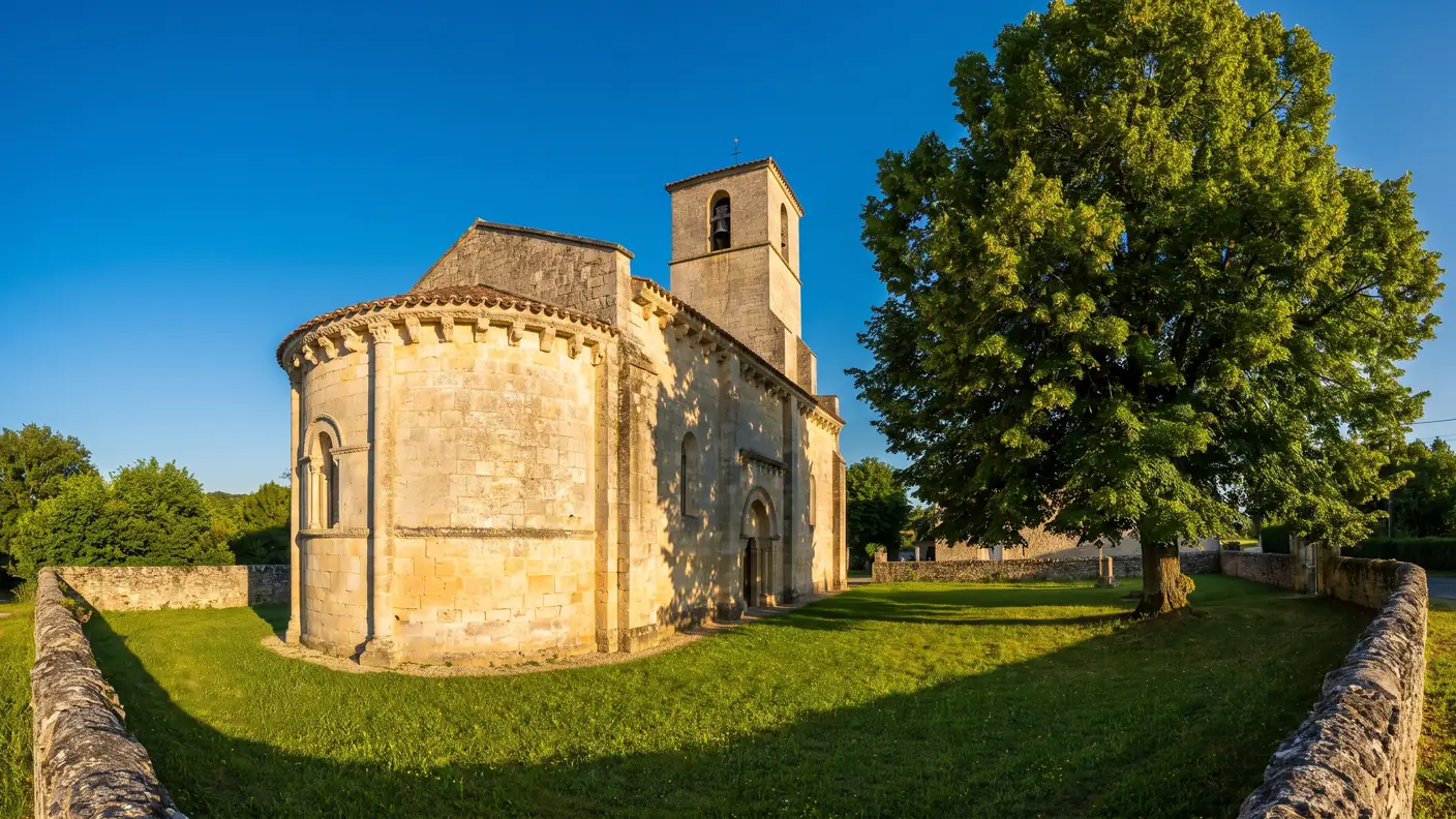 Une petite église romane du XIIe siècle en pierre couleur de miel, abside arrondie et clocher, dans un jardin