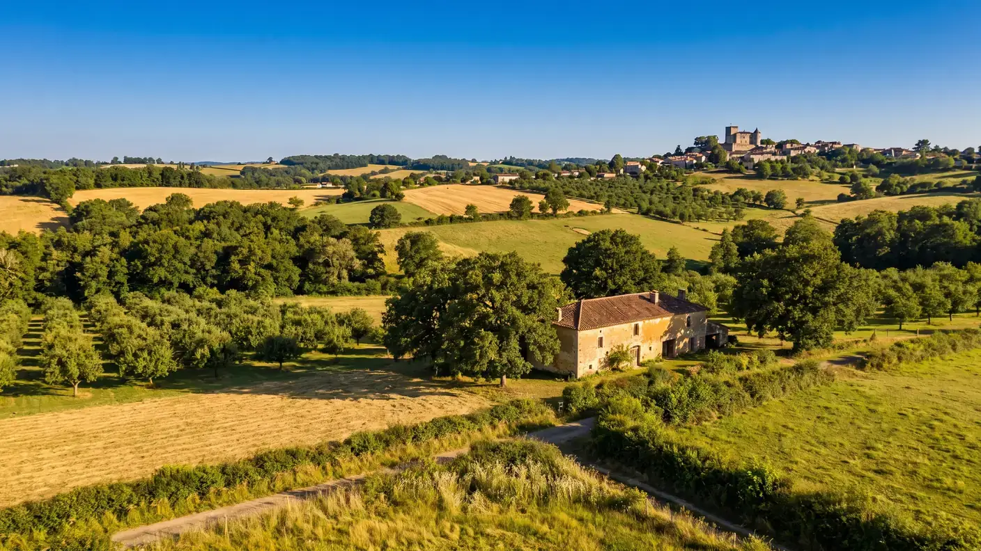 La campagne vallonnée de Guyenne autour de Lauzun, champs, vergers et bois, un village avec château au loin