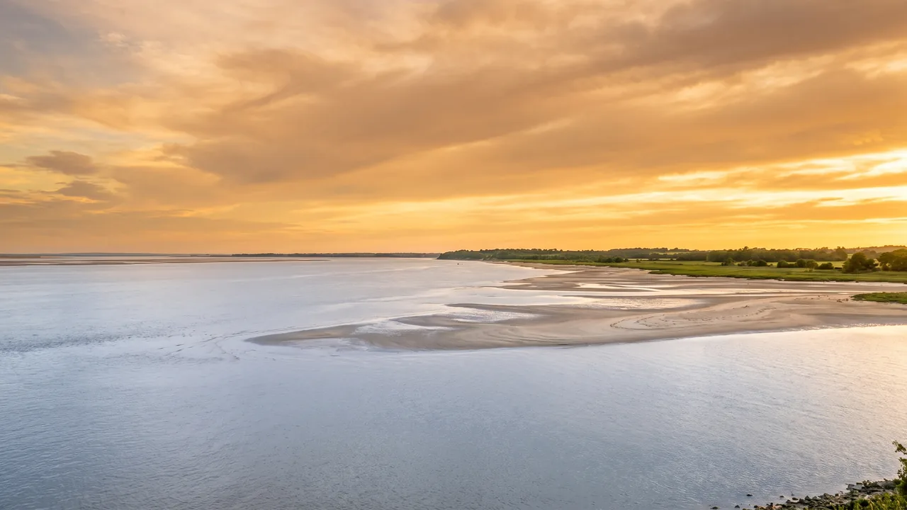 Vaste estuaire de la Gironde au soleil couchant, immense étendue d'eau calme argentée jusqu'à un rivage lointain