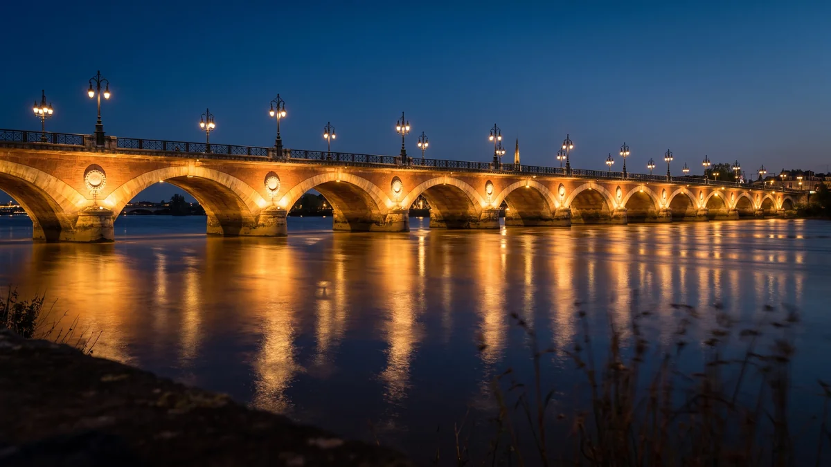 Berline VTC franchissant le Pont de pierre illuminé la nuit à Bordeaux