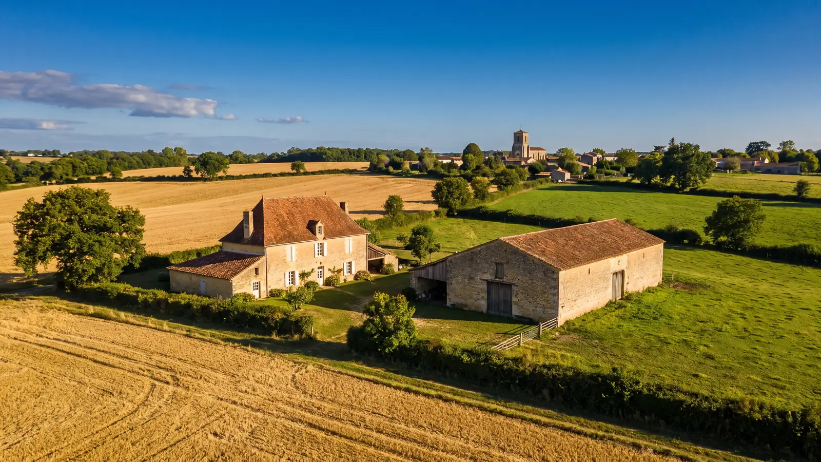 Une ferme de pierre et ses dépendances au milieu des champs et des prairies en Gironde en fin d'été, un clocher au loin