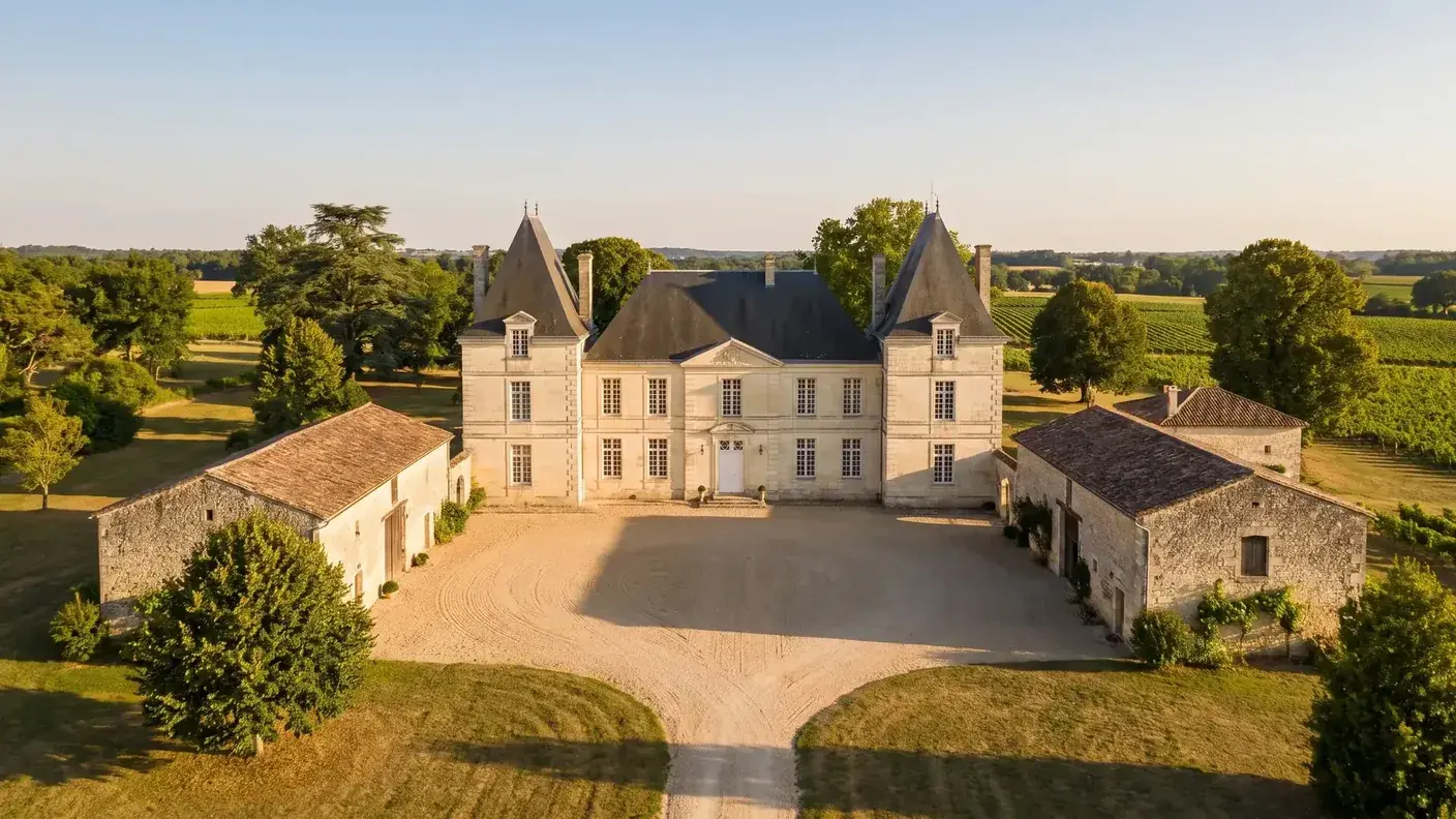 Logis viticole charentais en pierre de taille blonde entouré de vignes et de dépendances de ferme, toitures d'ardoise