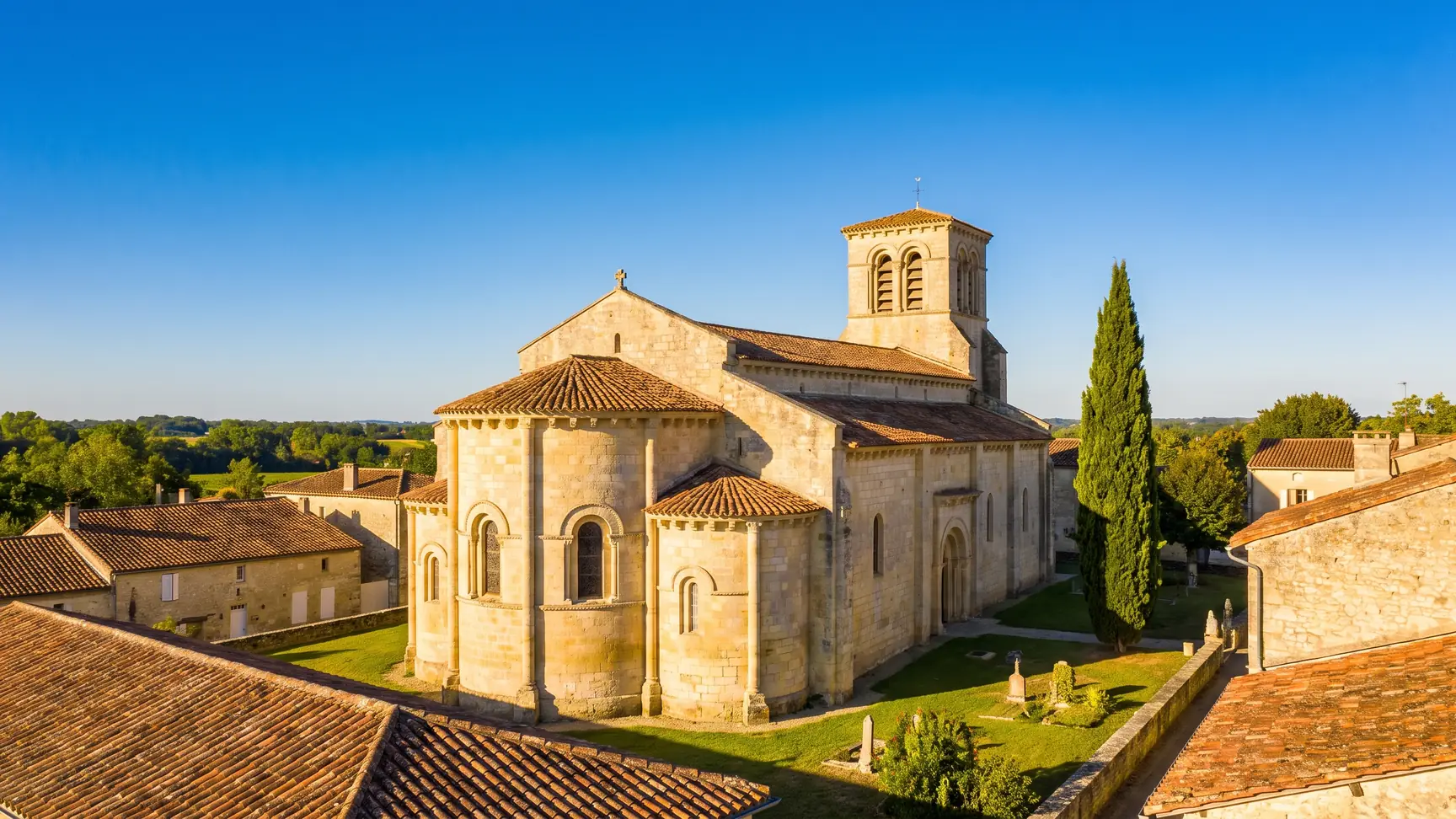 Une église romane de village en pierre dorée, chevet à absidioles et clocher dominant les toits, en Gironde