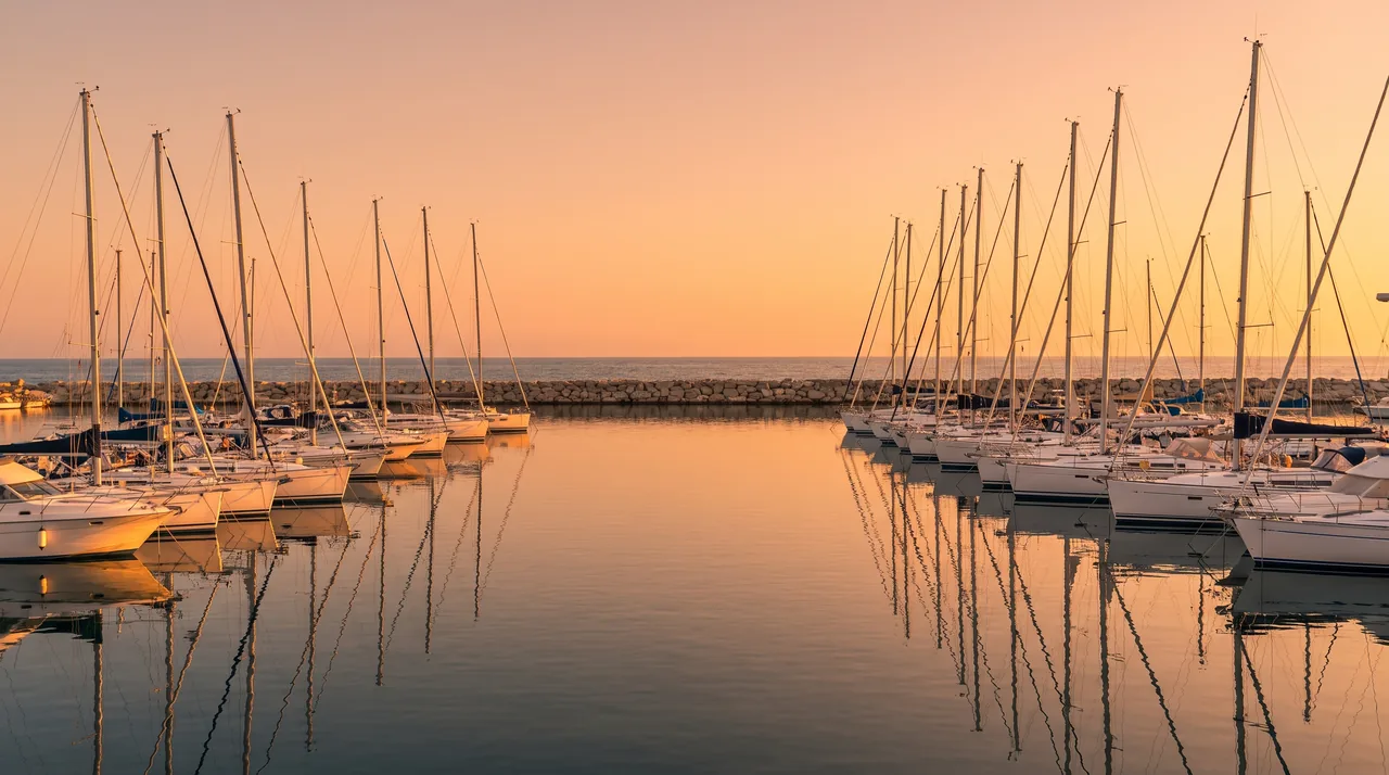 Le port de plaisance de Royan au soleil couchant, rangées de voiliers blancs amarrés sur une eau calme, quais clairs au loin