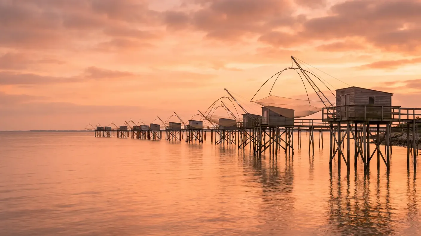 Des carrelets, cabanes de pêche sur pilotis au-dessus de l'estuaire de la Gironde au coucher du soleil