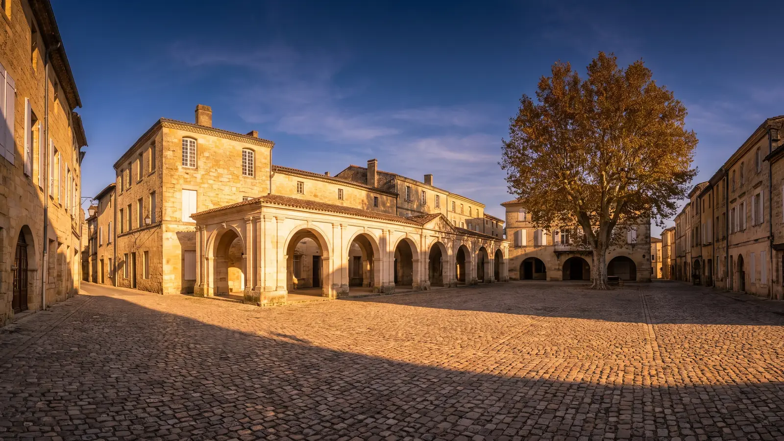 Une place médiévale bordée d'arcades de pierre jumelées et de maisons anciennes en Gironde, pavés et arcs en plein cintre