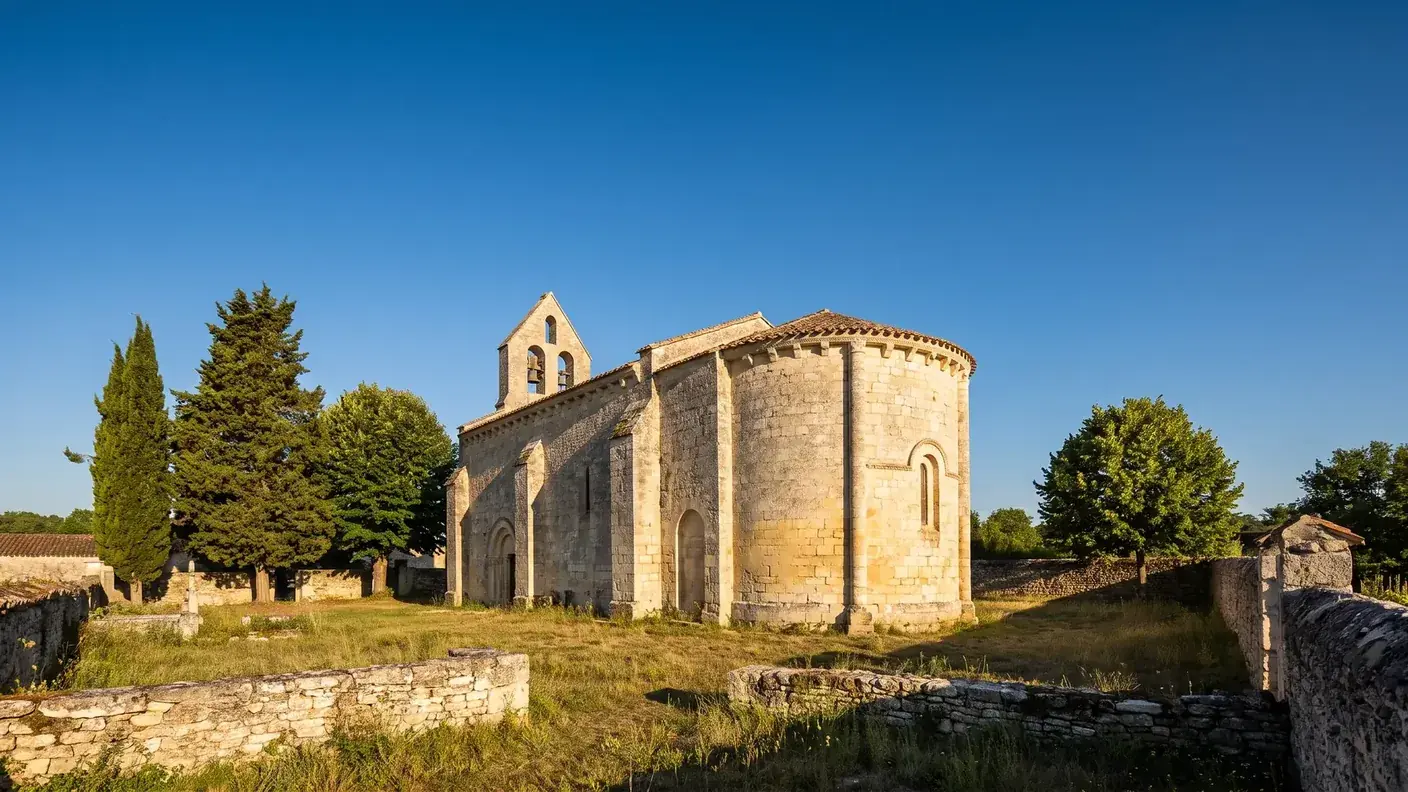 Une petite église romane saintongeaise en pierre calcaire claire, abside semi-circulaire à modillons, clocher