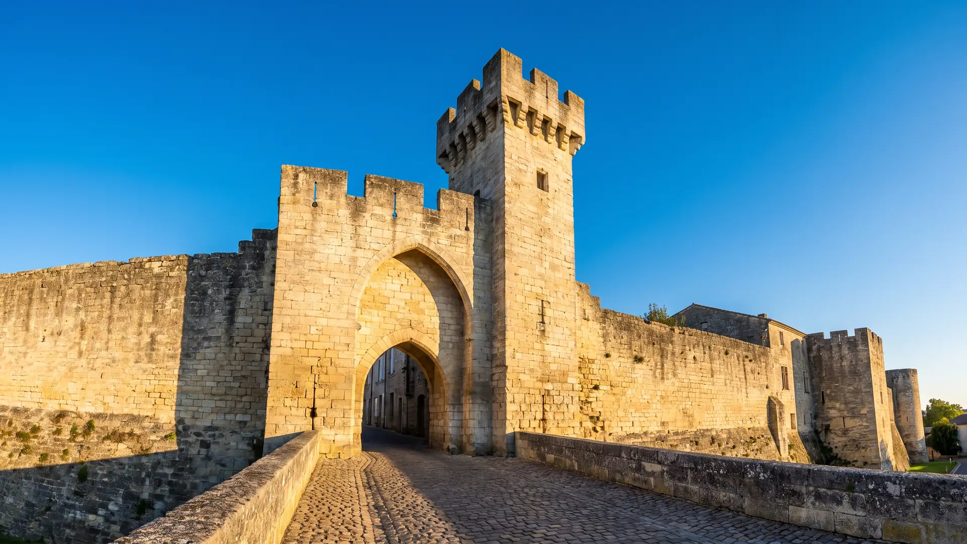 Une porte fortifiée médiévale en pierre claire flanquée d'une tour crénelée, à l'entrée d'une bastide en Gironde