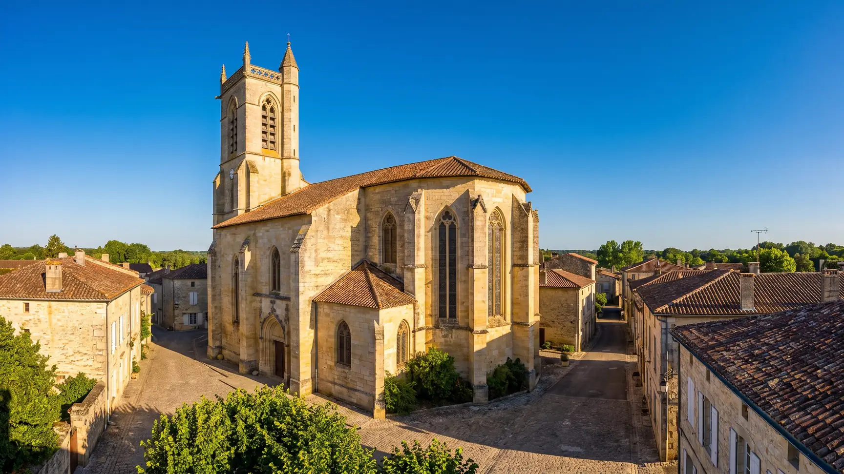 Une église gothique en pierre dorée dominant les toits de tuiles d'une bastide de l'Entre-deux-Mers, en Gironde