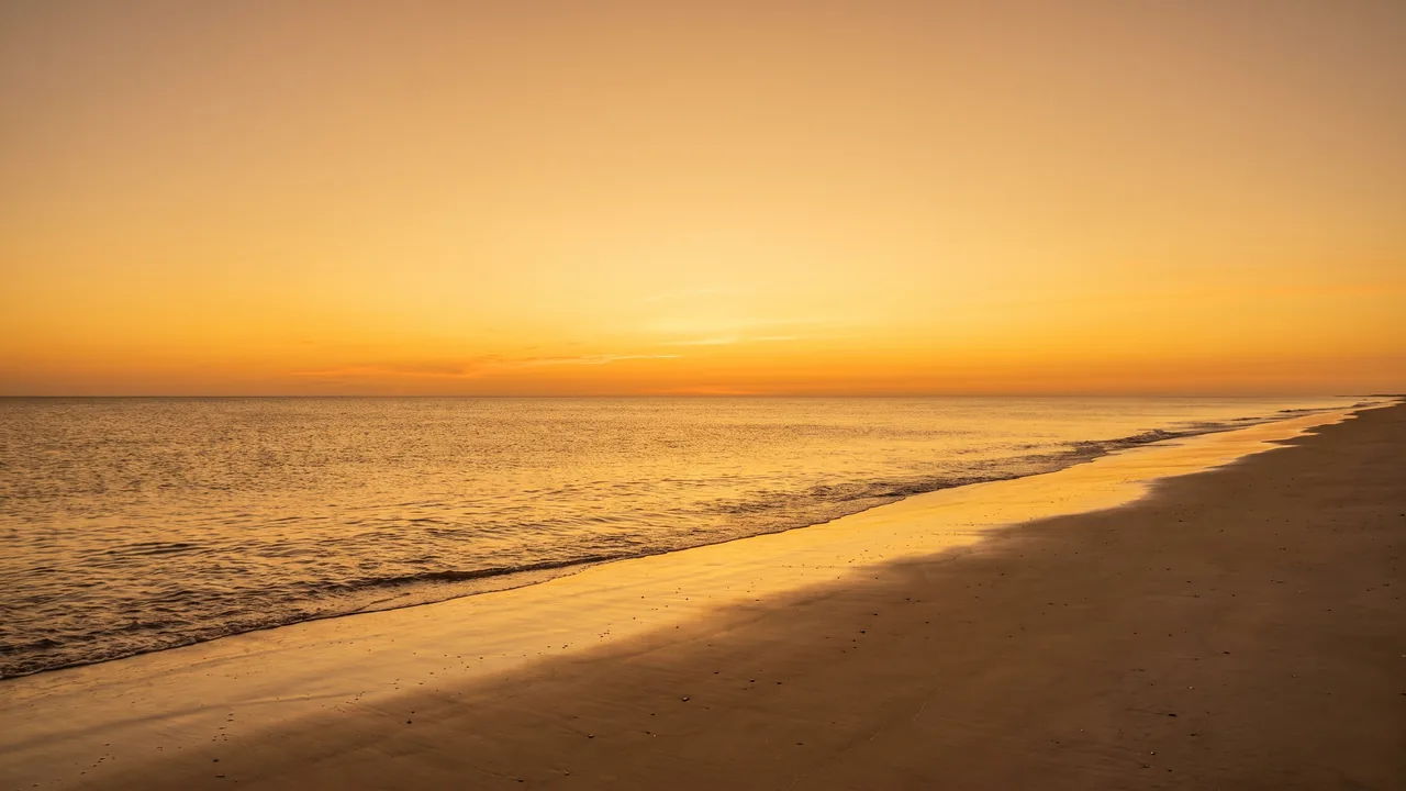 Coucher de soleil orangé sur l'horizon de l'Atlantique depuis une plage déserte de Soulac