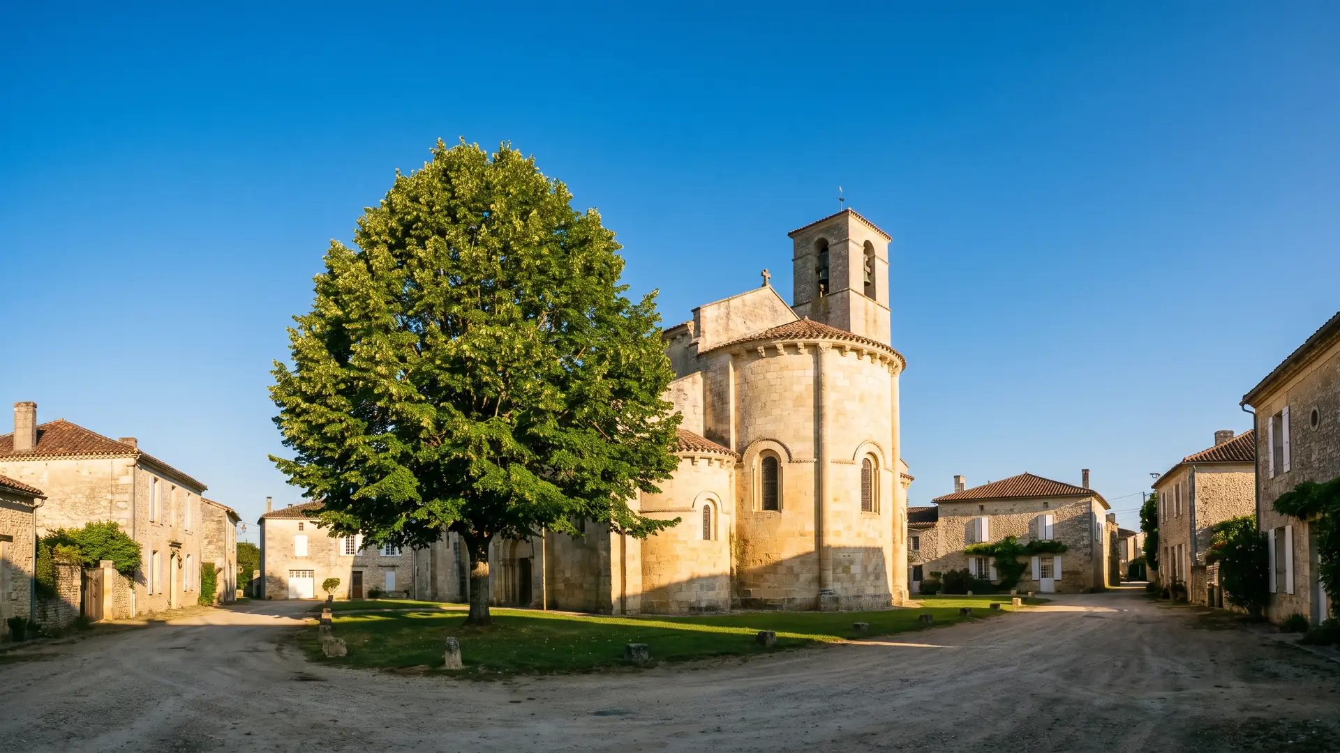 Une église romane de village en pierre dorée, chevet et clocher dominant les toits de tuiles, en Gironde